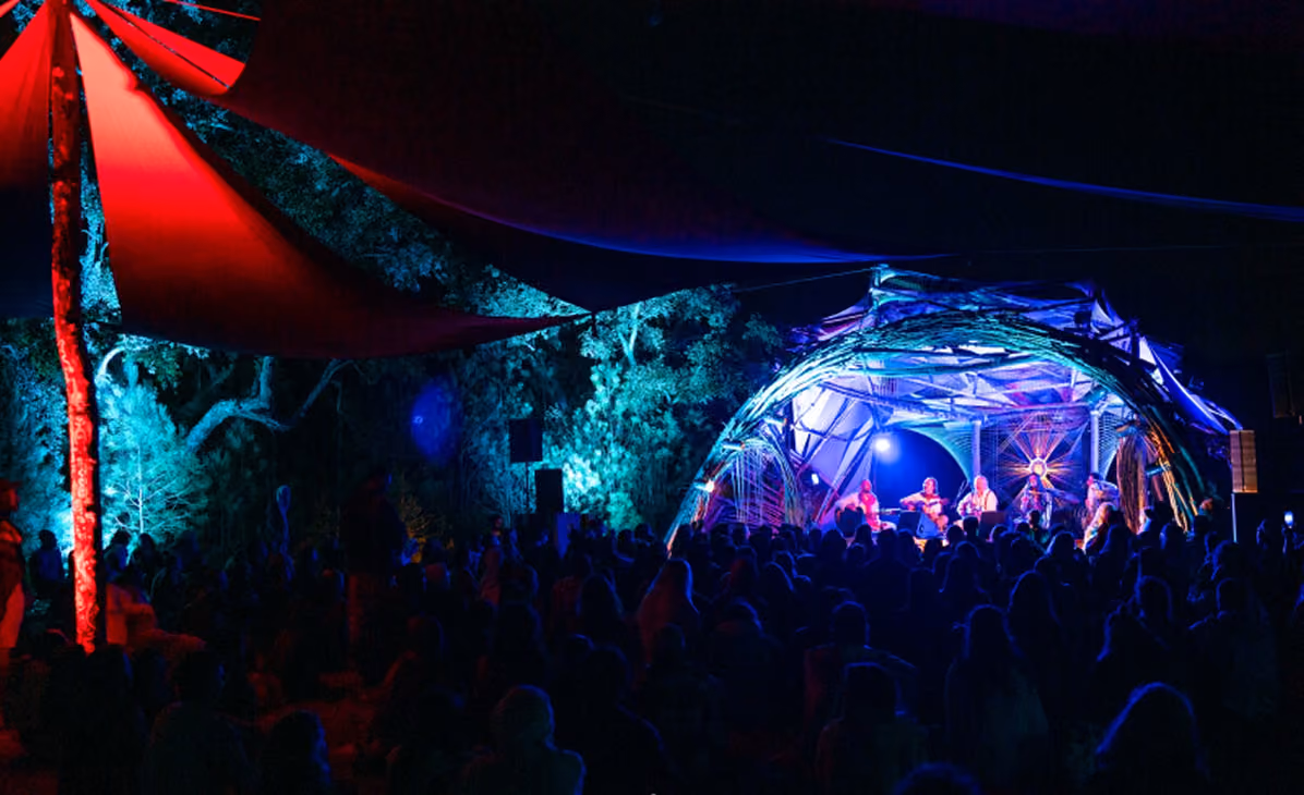 A bearded man singing into a microphone with stage lights behind, promoting Ape Chimba at Icaros Medicine Music Festival in Sesimbra, Portugal, August 21-23, 2026.