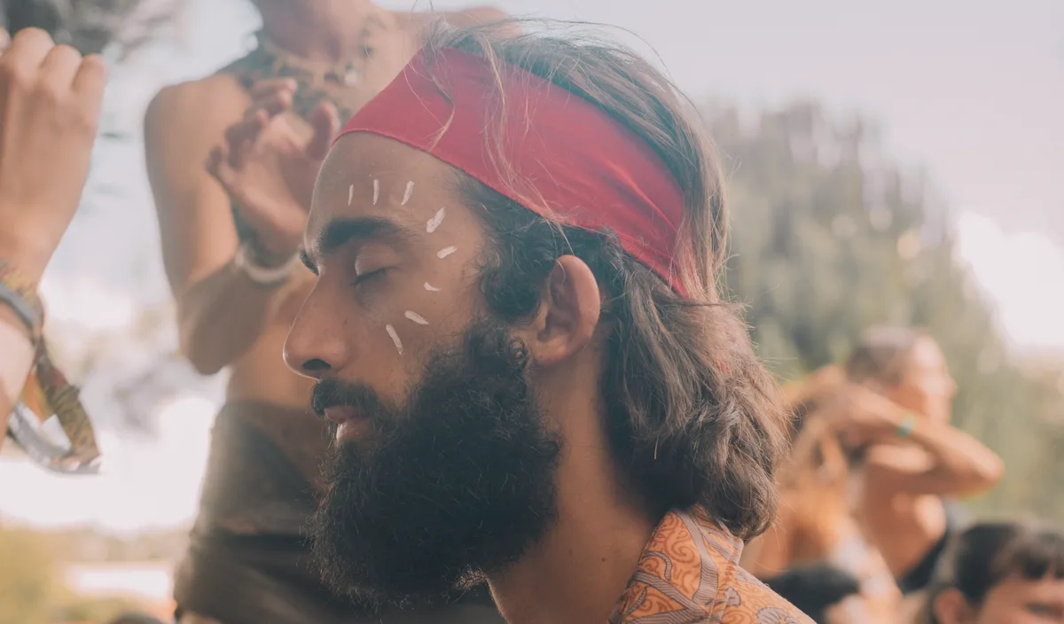 Tiago with his eyes closed in a ceremony circle, a red band on his head and white paint on his face.