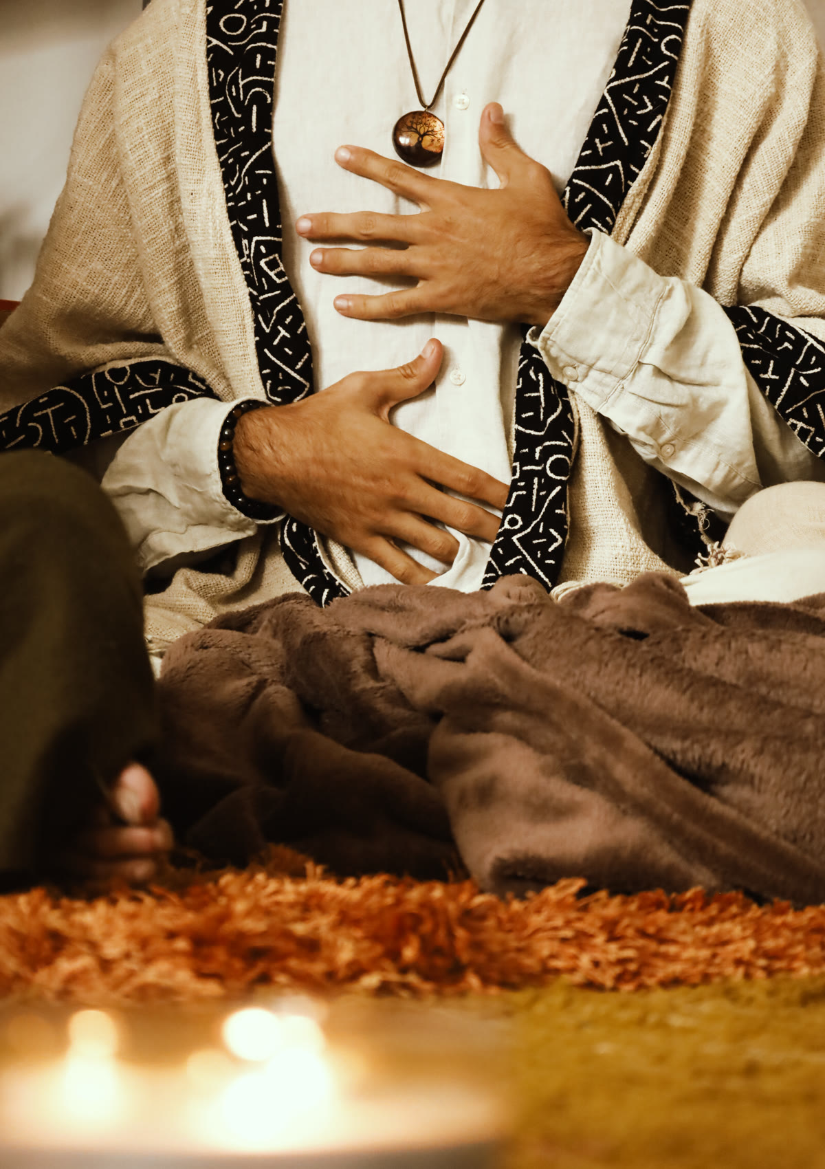 Tiago sitting in a ceremony robe, one hand on his chest and one on his belly, candles in front of him