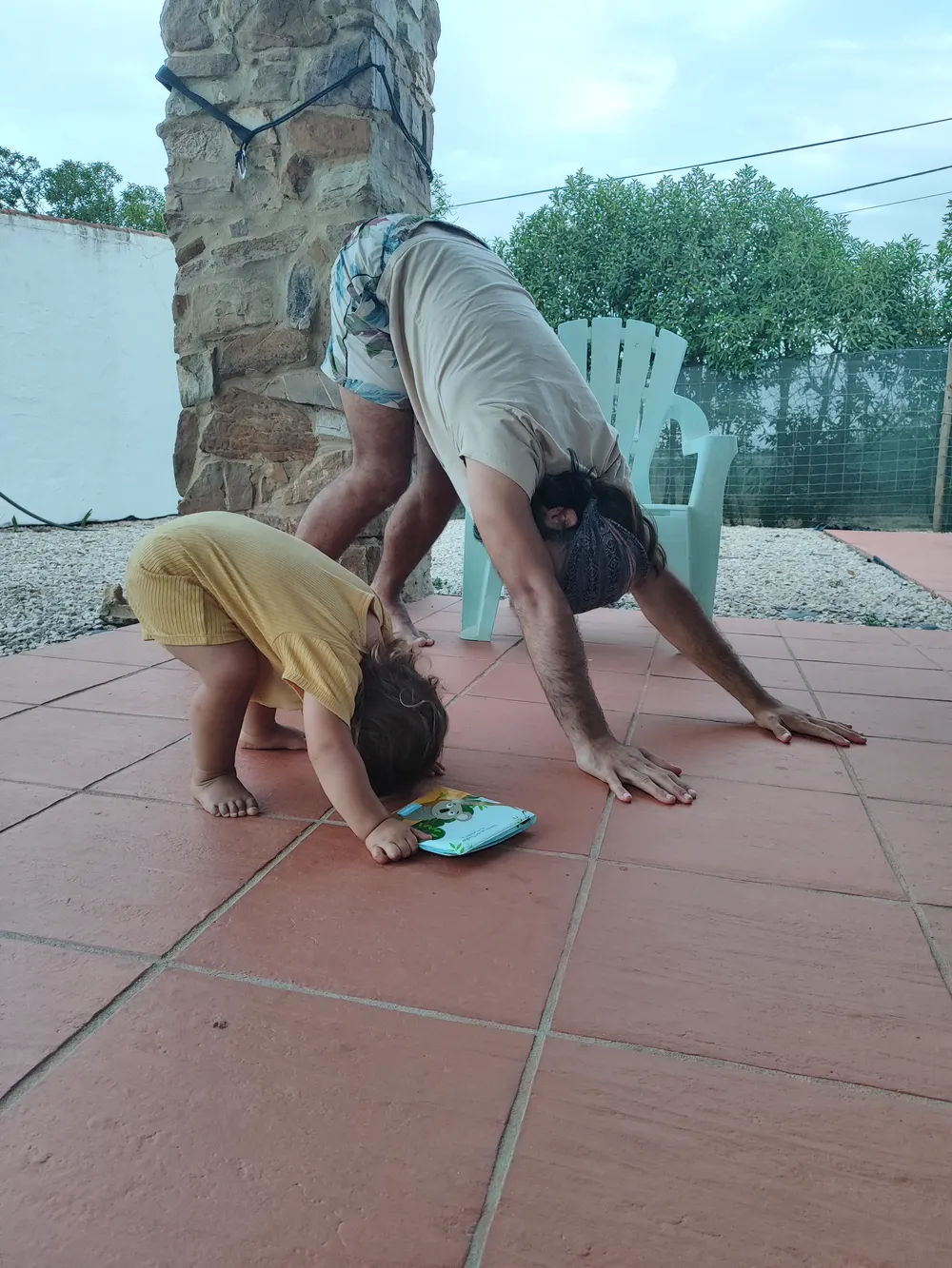 Tiago in a downward dog on a terrace, his son copying him at his side.